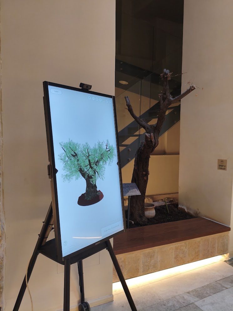 The Guestbook touchscreen standing beside the olive tree in the Dar Al Consul courtyard
